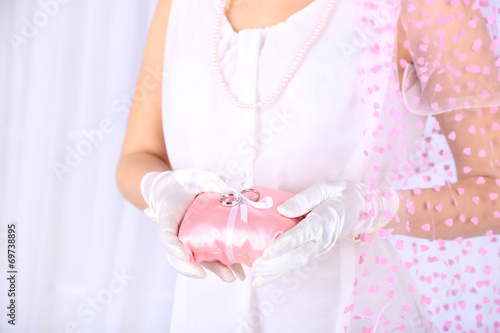 Bride in white dress and gloves holding decorative pillow with