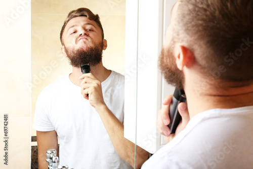 Young man shaving his beard in bathroom