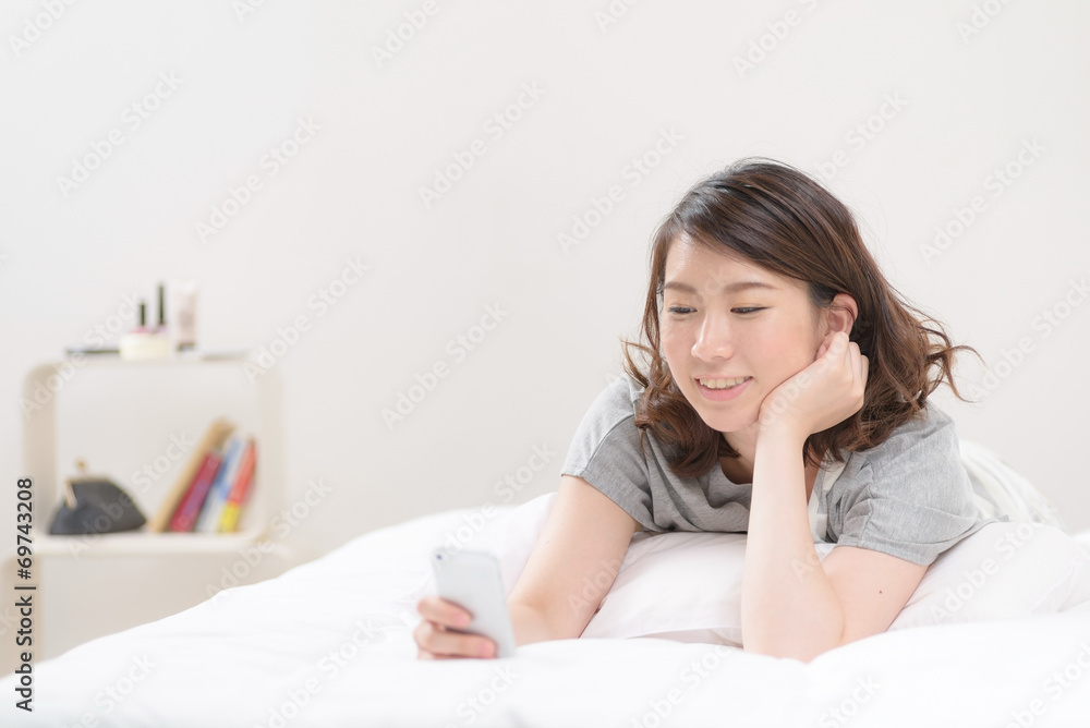 ベッドにうつ伏せでスマートフォンを使う女性