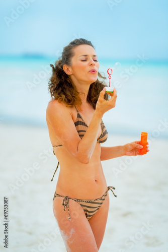 Portrait of young woman blowing soap bubbles on beach