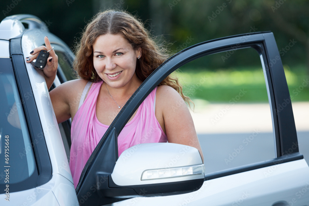 Smile woman with car key in hand stands near vehicle opened door