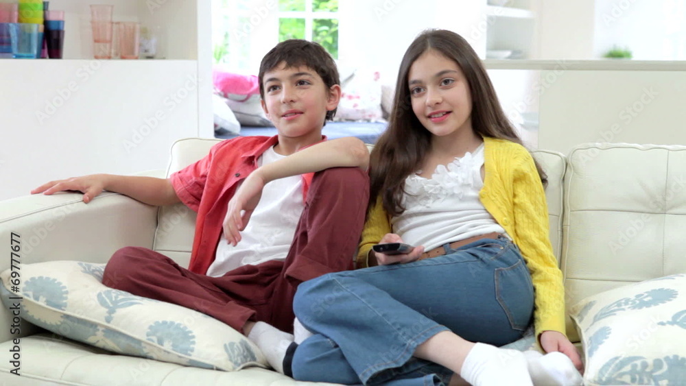 Two Hispanic Children Sitting On Sofa Watching TV Together