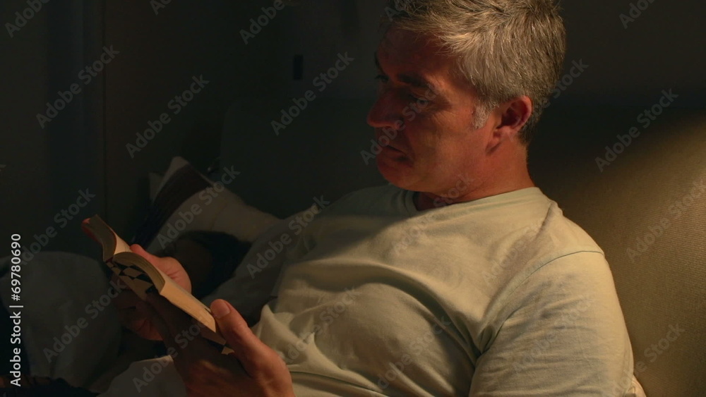 Middle Aged Couple In Bed With Man Reading Book Middle Aged Couple In Bed With Man Reading Book