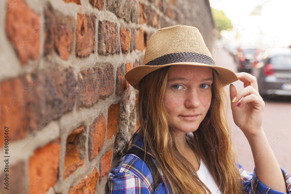 Pretty young girl in hat near a brick wall on the street.