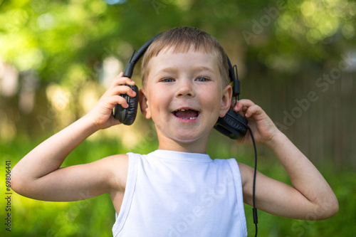 Funny little boy enjoying music in headphones outdoors.