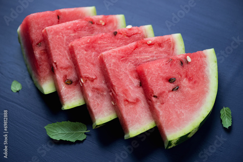 Sliced watermelon with fresh mint, dark blue wooden background