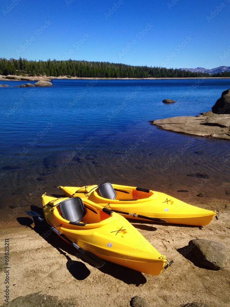 Fototapeta premium Two yellow kayaks on the shore of a beautiful lake.