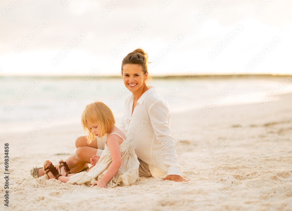 Happy mother and baby girl sitting on the beach in the evening Happy mother and baby girl sitting on the beach in the evening