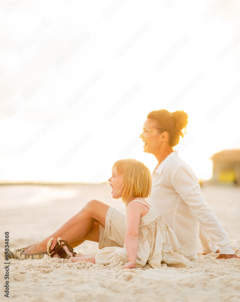 Happy baby girl and mother sitting on the beach in the evening Happy baby girl and mother sitting on the beach in the evening