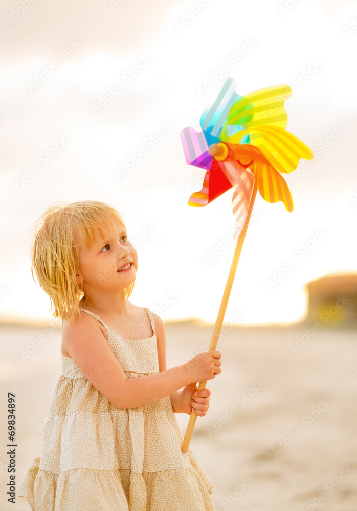 Baby girl playing with colorful windmill toy on the beach Baby girl playing with colorful windmill toy on the beach