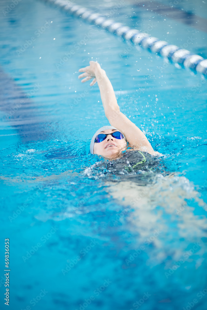 Young girl in goggles swimming back crawl stroke style