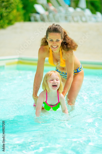 Portrait of happy mother and baby girl playing in swimming pool