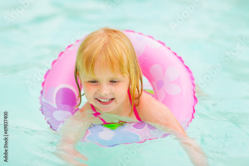 Portrait of baby girl with swim ring swimming in pool