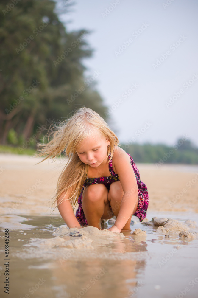 Fototapeta premium Adorable girl play with wet sand on sunset ocean beach