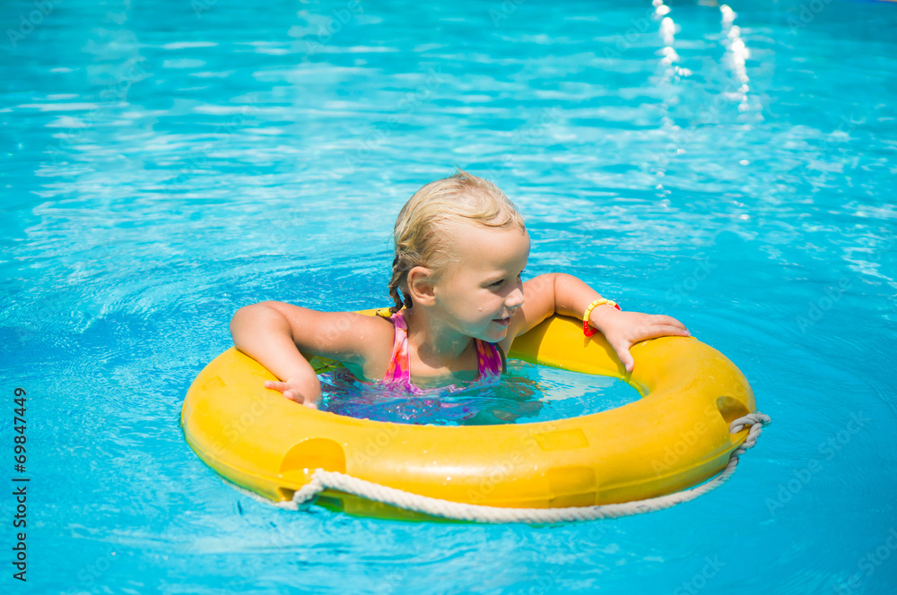 Adorable girl swim on yellow life ring in pool at protical beach