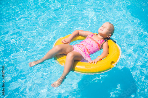 Adorable girl relax on yellow life ring in pool at protical beac