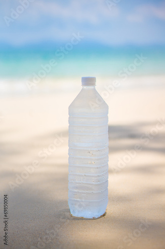 Cold water bottle with drops on it on tropical island beach