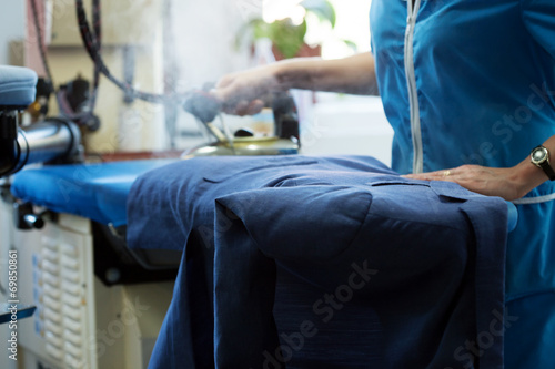 Obraz na plátně Laundry worker steaming jacket on ironing board