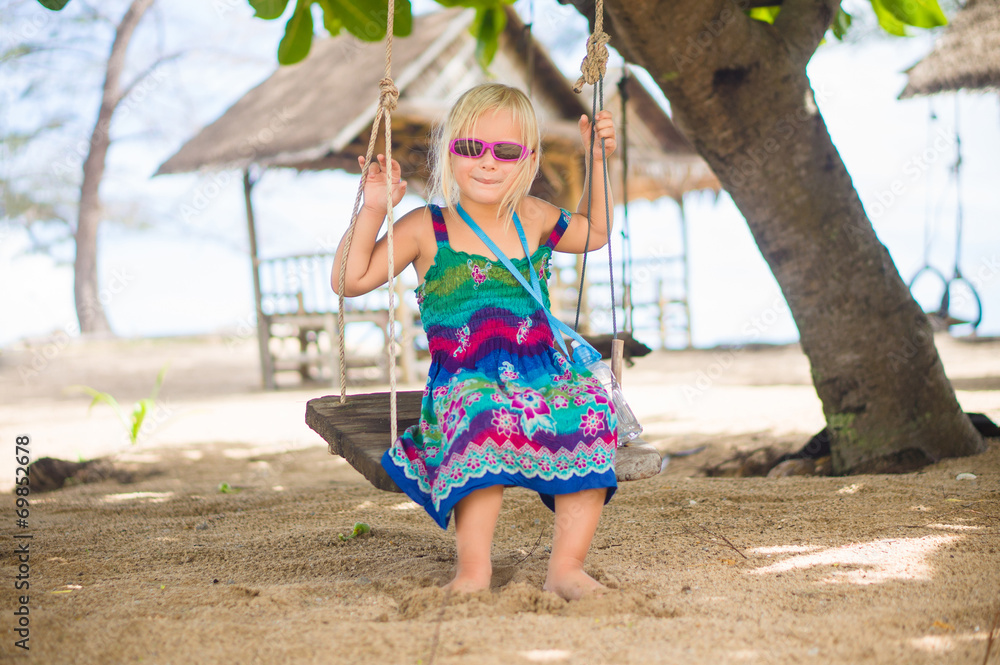 Adorable girl in sunglasses sit on rope swing under palm trees o Adorable girl in sunglasses sit on rope swing under palm trees o