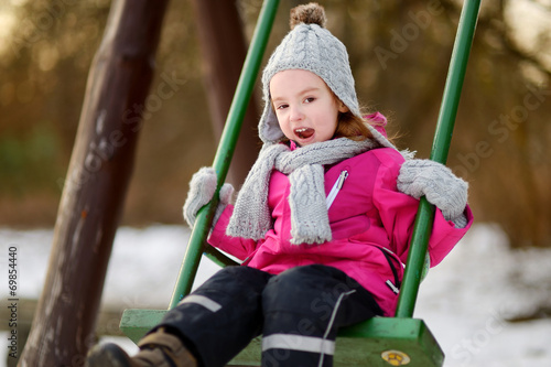 Adorable girl having fun on a swing on winter day © MNStudio