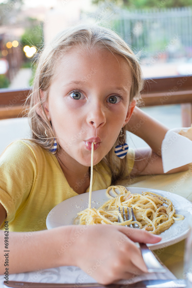 Adorable little girl eating spaghetti in outdoors restaraunt