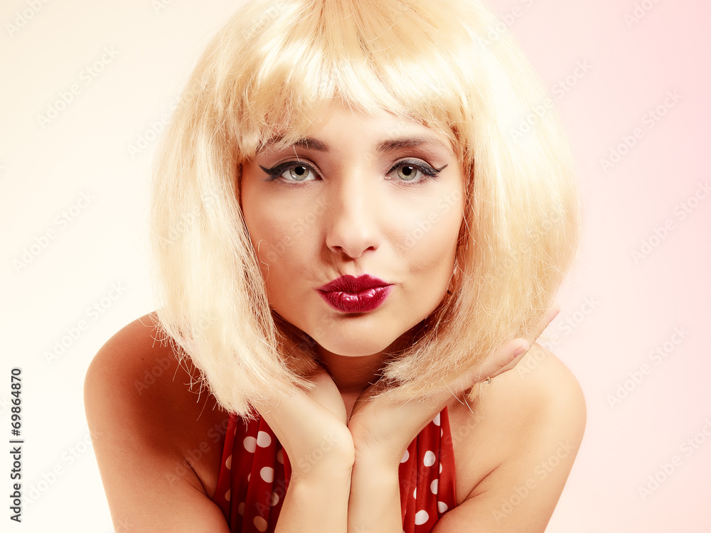 Fototapeta premium Pinup girl in blond wig retro dress blowing a kiss