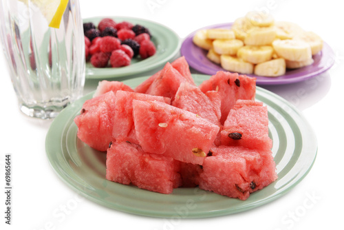 Sliced fruits and berries on plate with glass of water close up