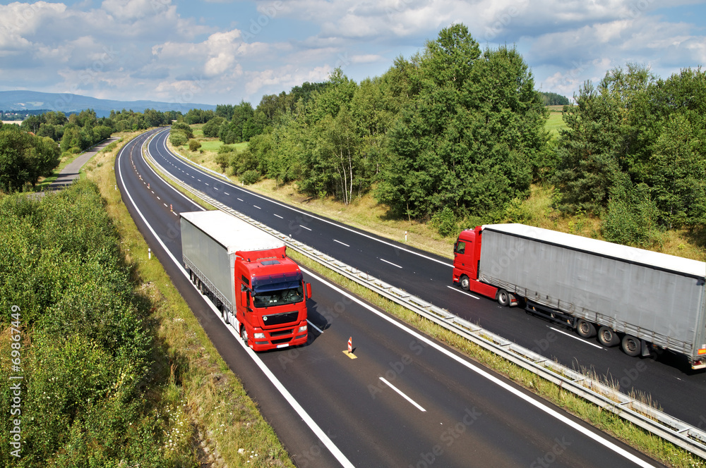 Rural landscape with trees lined the highway, two red trucks