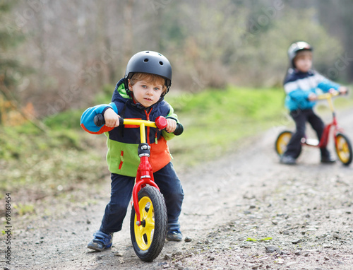 Two active little sibling boys having fun on bikes in forest