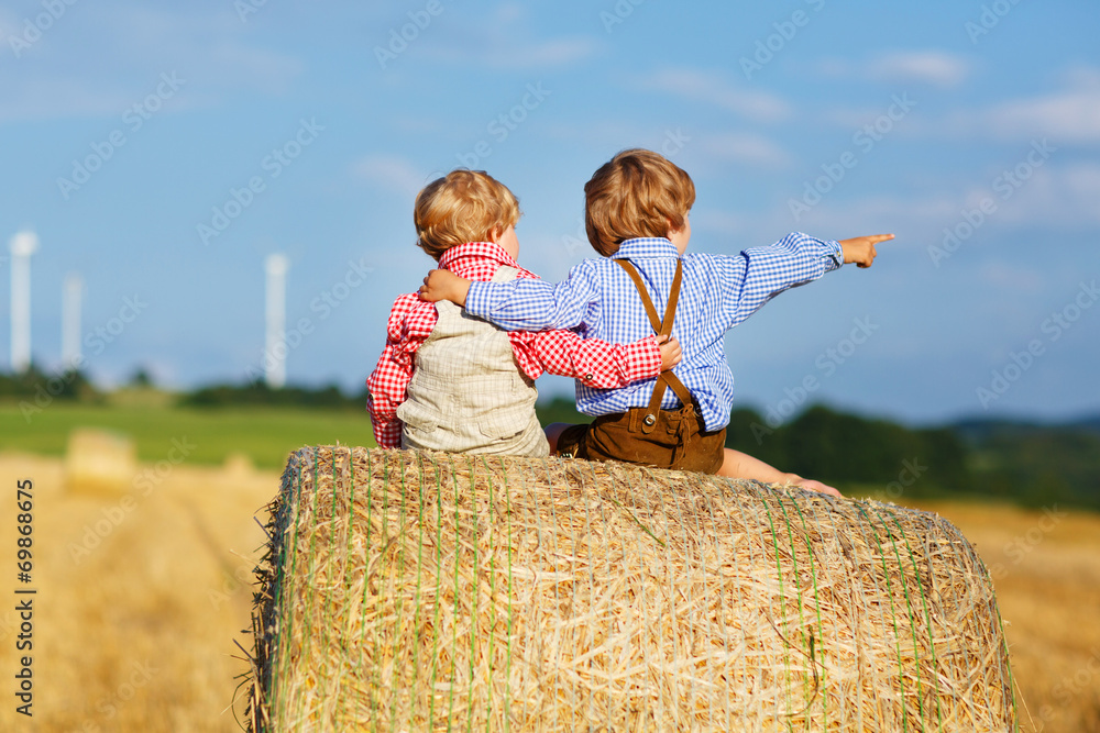 Obraz premium Two little twin boys and friends sitting on hay stack