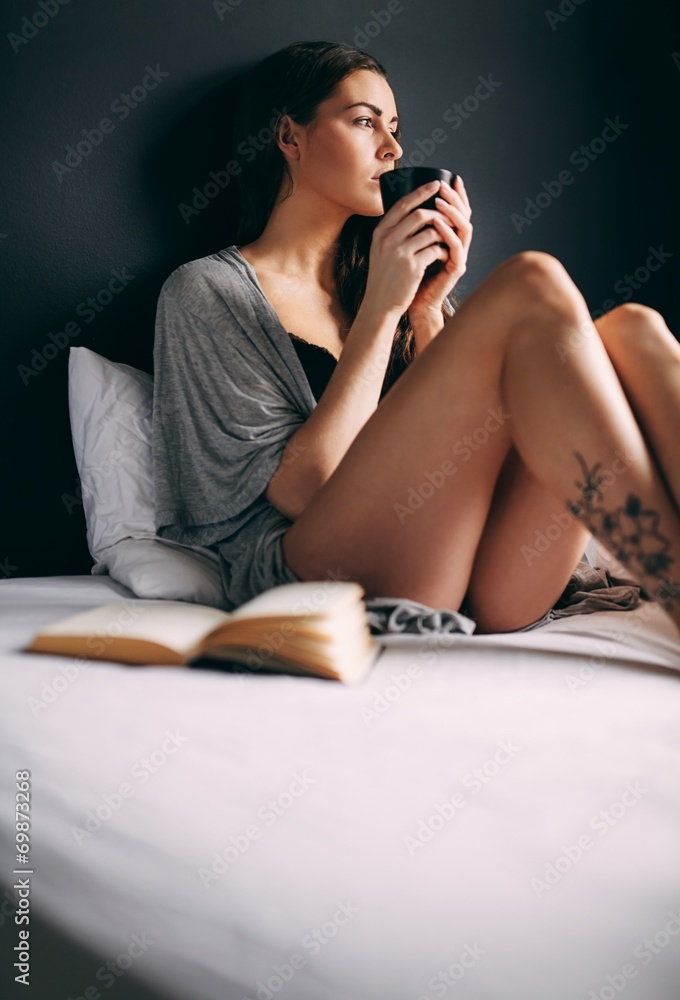 Naklejka premium Young lady on bed drinking coffee looking away thinking