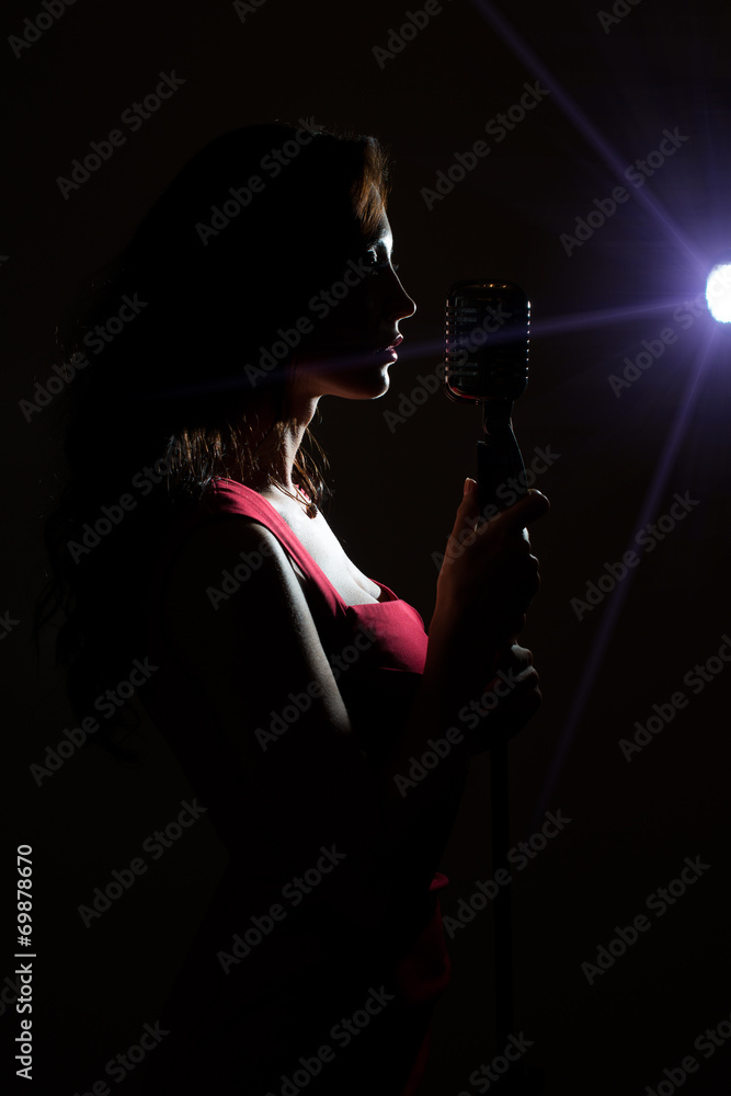 Obraz premium Silhouette of woman singing into vintage microphone.