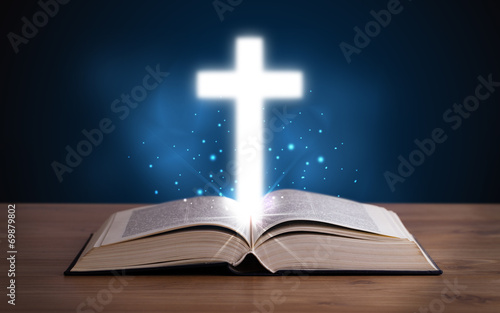 Open holy bible with glowing cross in the middle