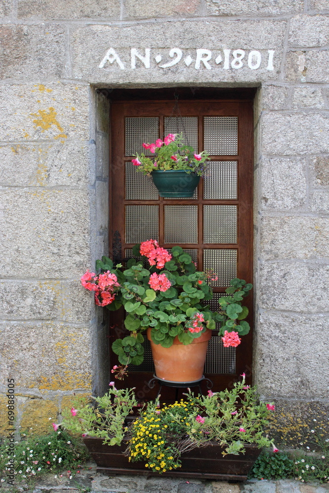 Ancienne maisone en pierre à Pont-Croix, Brategne, France. Pot de fleurs de geranium devant la port. Ancienne maisone en pierre à Pont-Croix, Brategne, France. Pot de fleurs de geranium devant la port.