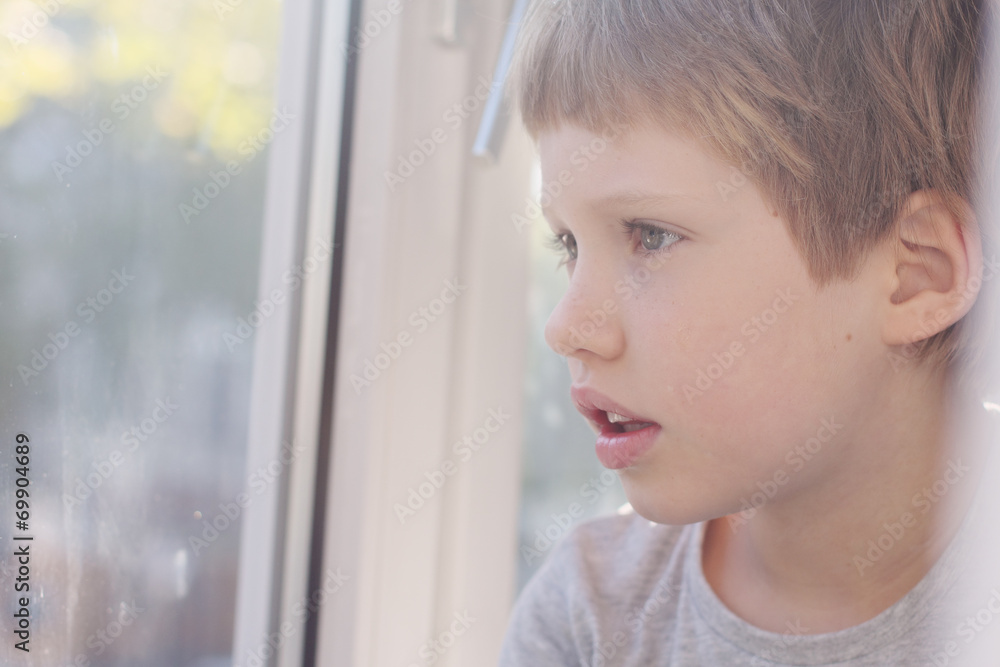 Cute 6 years old boy looking through the window Cute 6 years old boy looking through the window