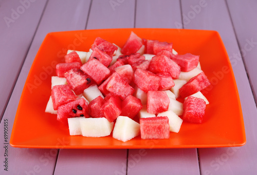 Slices of watermelon in orange plate on wooden background