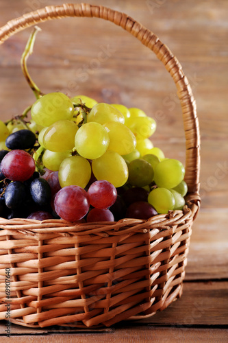 Different kinds of grapes in wicker basket on wooden background