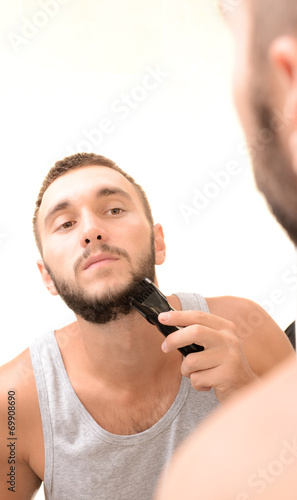 Young man shaving his beard in bathroom