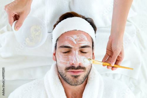 Man with clay facial mask in beauty spa. #69911281