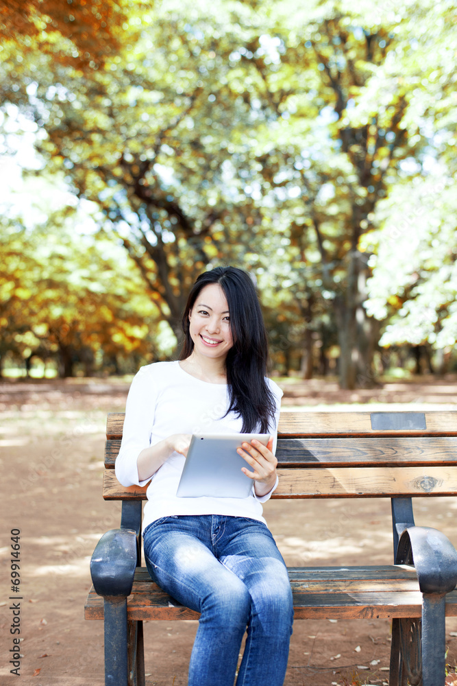 Obraz premium 公園のベンチでタブレットPCを使う女性