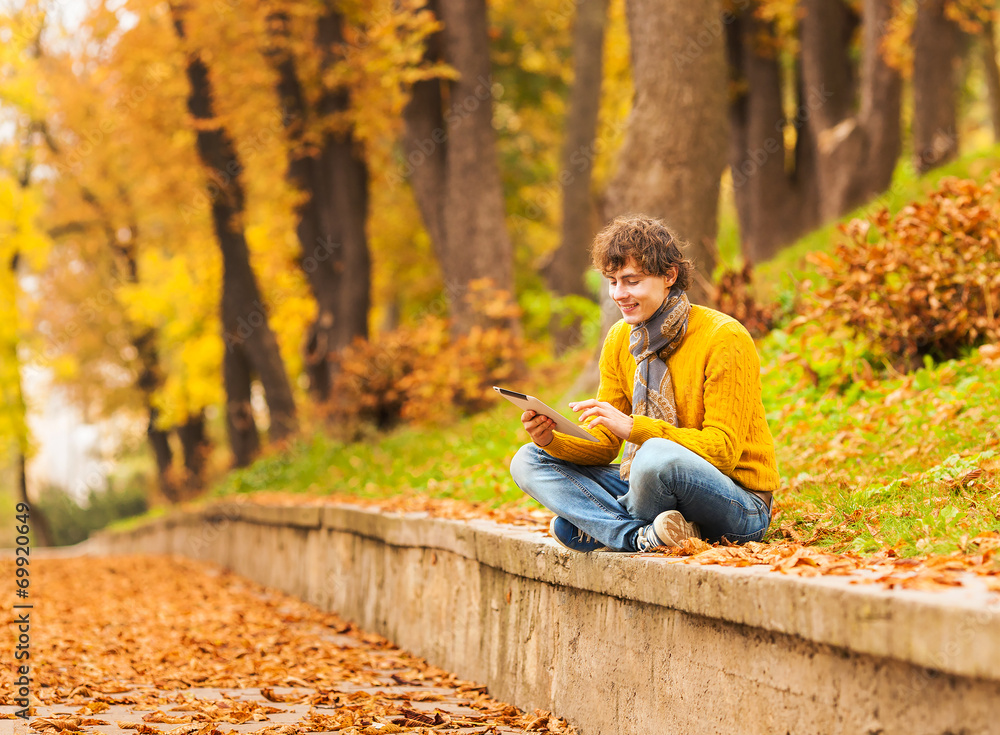 curly man with computer tablet in autumn park curly man with computer tablet in autumn park