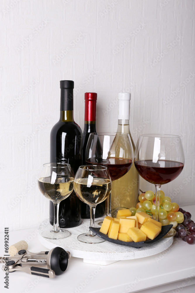 Obraz premium Assortment of red and white wine bottles with glasses, cheese cubes, and grapes on a white wooden tray