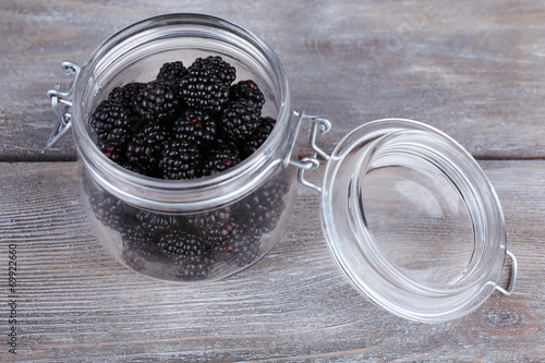 Sweet blackberries in glass jar on wooden background