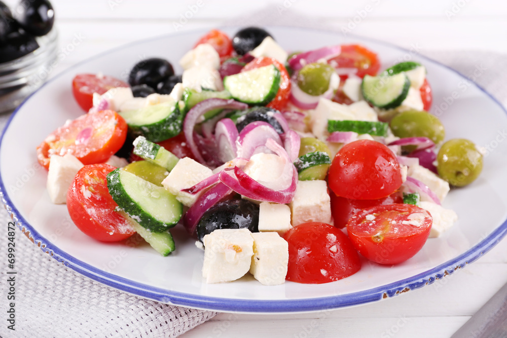 Greek salad served in plate on napkin on wooden background