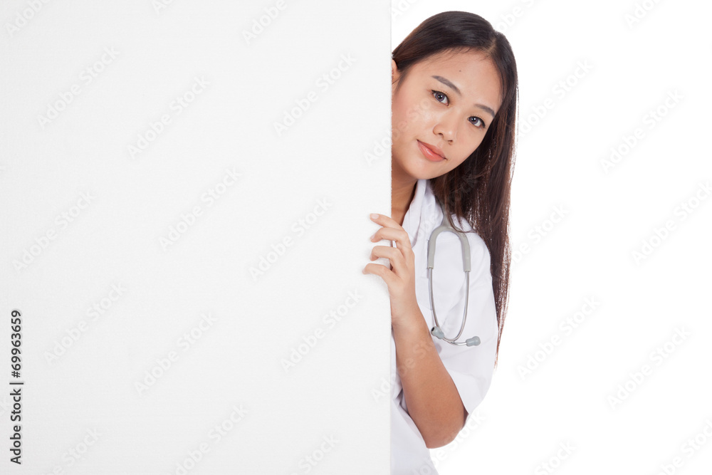Young Asian female doctor peeking from behind blank sign billboa Young Asian female doctor peeking from behind blank sign billboa