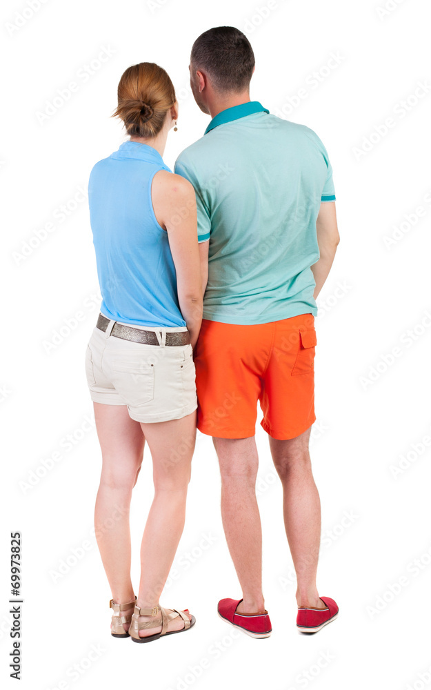 Back view of young embracing couple in shorts hug and look. Back view of young embracing couple in shorts hug and look.