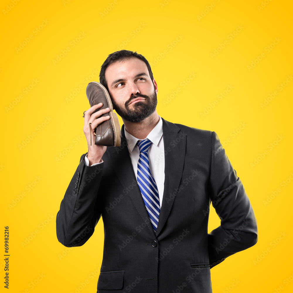 Young businessman talking to his shoe over yellow background Young businessman talking to his shoe over yellow background