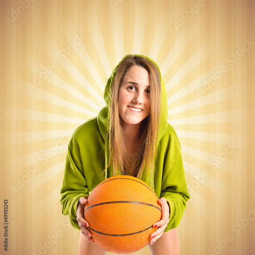 Blonde girl playing basketball over ocher background