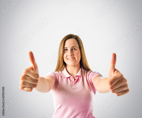Young girl making Ok sign over grey background © luismolinero