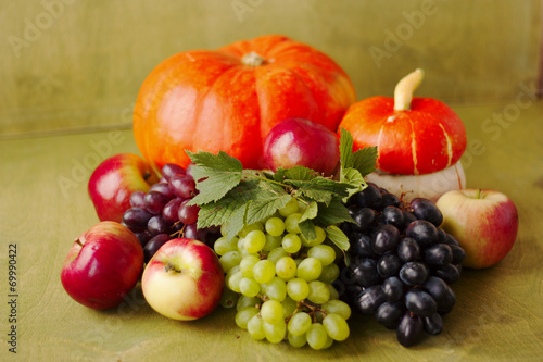 one pumpkin, apples, grapes on a green wooden background